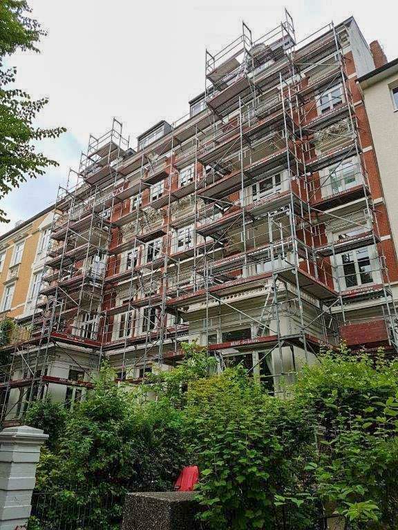 Die Gebäudefassade ist wegen Renovierungsarbeiten eingerüstet. Rote Ziegel und weiße Zierelemente sind sichtbar.