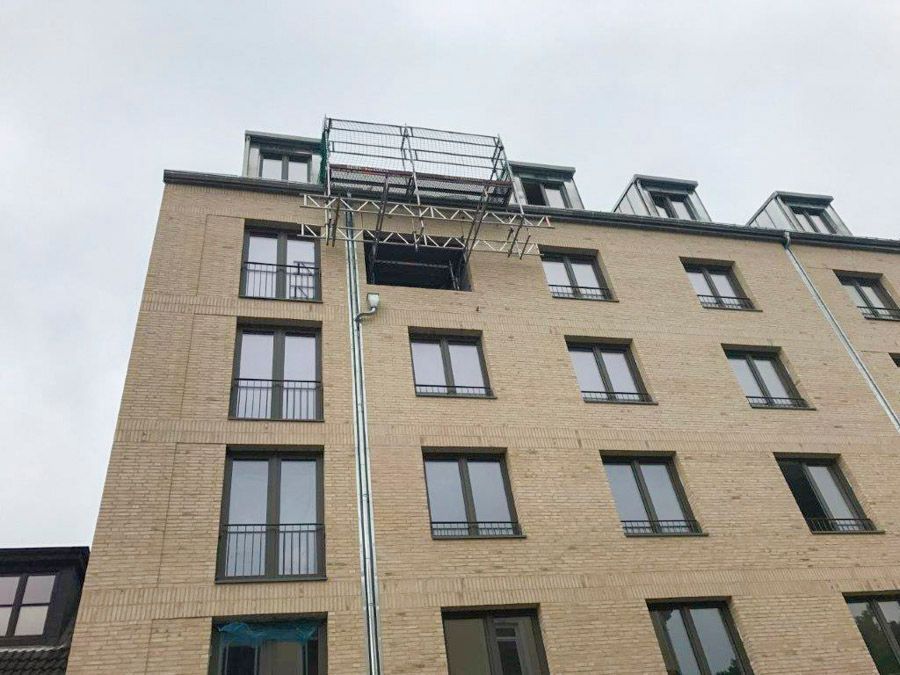 Unter bewölktem Himmel ist an einem Fenster eines mehrstöckigen Backsteingebäudes eine bewegliche Hebebühne aufgebaut.