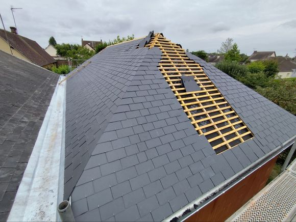 Des tuiles de toit en céramique rouge sont posées sur un toit, un ouvrier se trouvant en arrière-plan sous un ciel bleu.