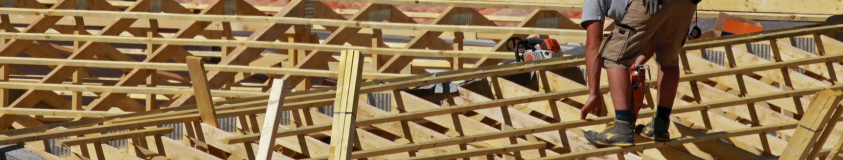 Un ouvrier du bâtiment travaille sur une charpente de toit en bois, avec des treillis et des supports détaillés, probablement celle d'un nouveau bâtiment.