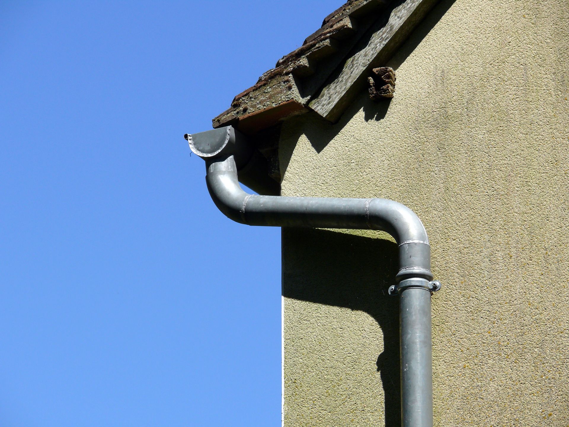 Système de gouttière en métal gris sur un bâtiment, se détachant sur un ciel bleu.