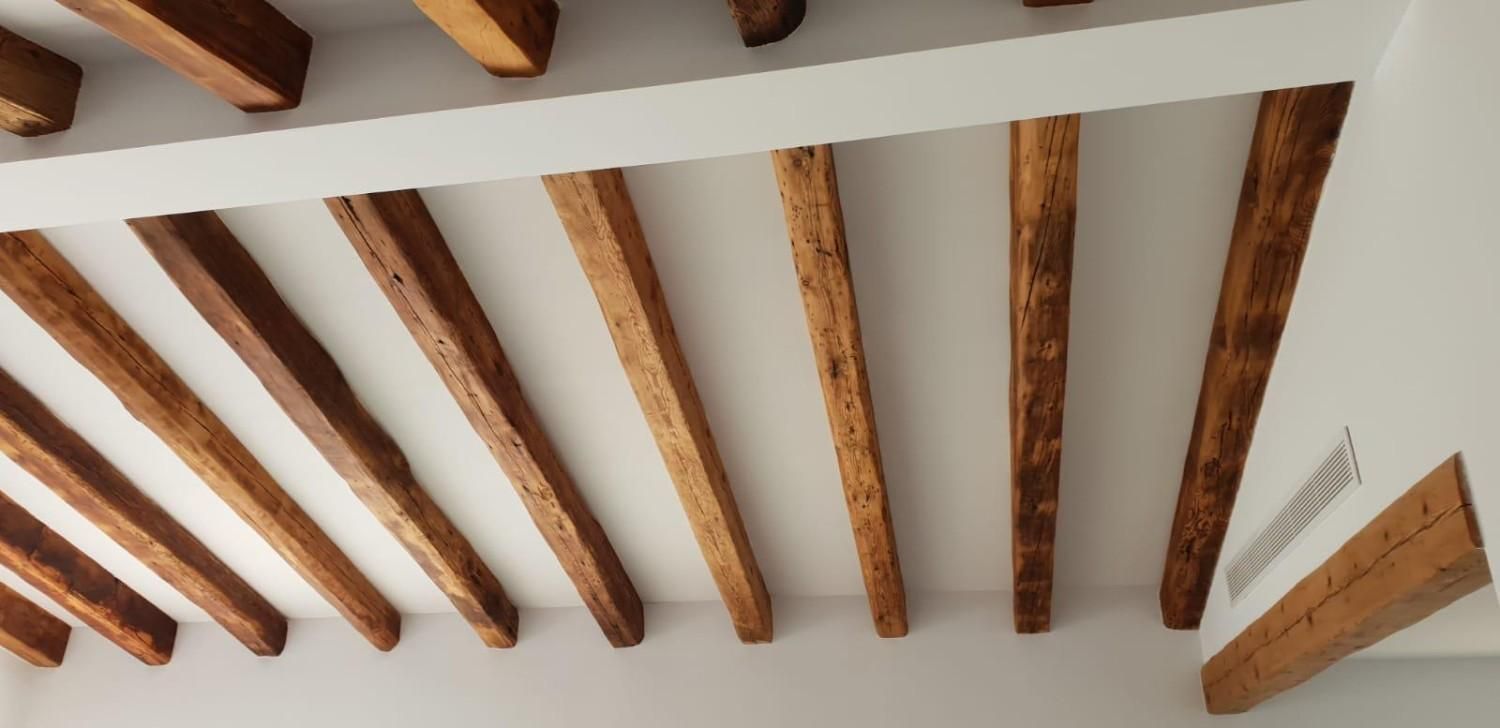 Una vista de ángulo bajo de un techo blanco con varias vigas de madera rústicas paralelas y una viga principal perpendicular.