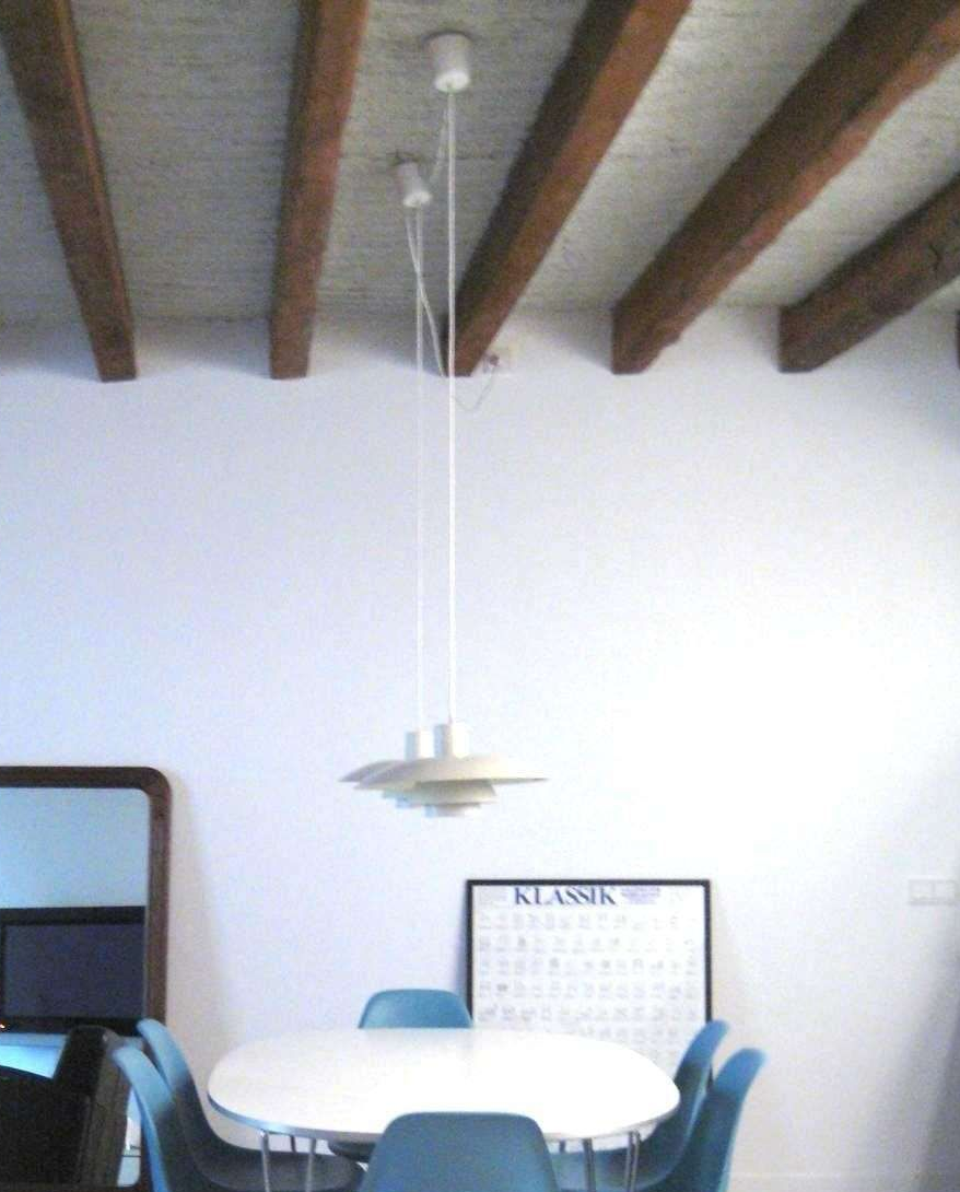 Un comedor con una mesa redonda blanca, sillas azules, una lámpara colgante y vigas de madera a la vista en el techo.