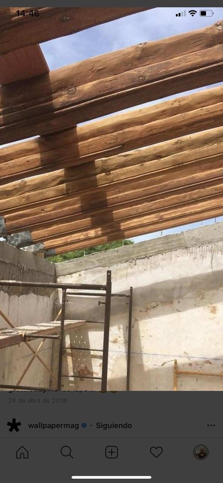 Interior de una obra en construcción que muestra vigas de madera expuestas que descansan sobre una pared.