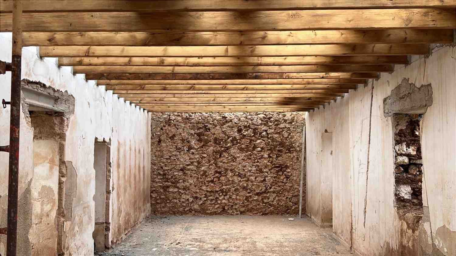 El interior de un edificio en construcción sin terminar, con vigas de madera a la vista en el techo y una pared.