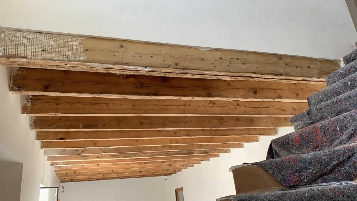 Una hilera de vigas de madera expuestas en el techo vistas desde un ángulo junto a una escalera alfombrada.