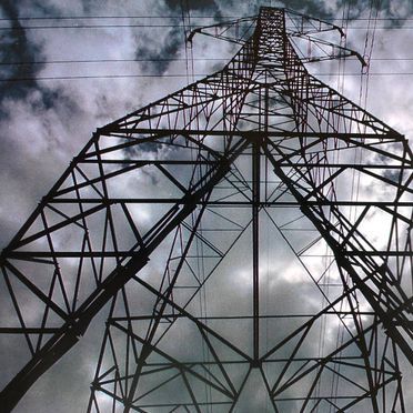 Mirando hacia arriba a una torre de energía con un cielo nublado en el fondo