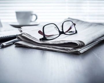 Un par de gafas están encima de un periódico sobre una mesa.