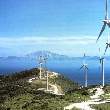 Una hilera de turbinas eólicas en la cima de una colina con vistas al océano.