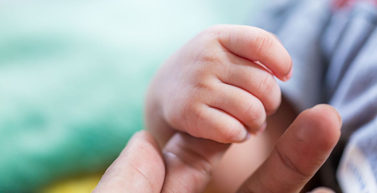 Petite main de bébé saisissant un doigt d'adulte, gros plan, mise au point douce, intérieur.