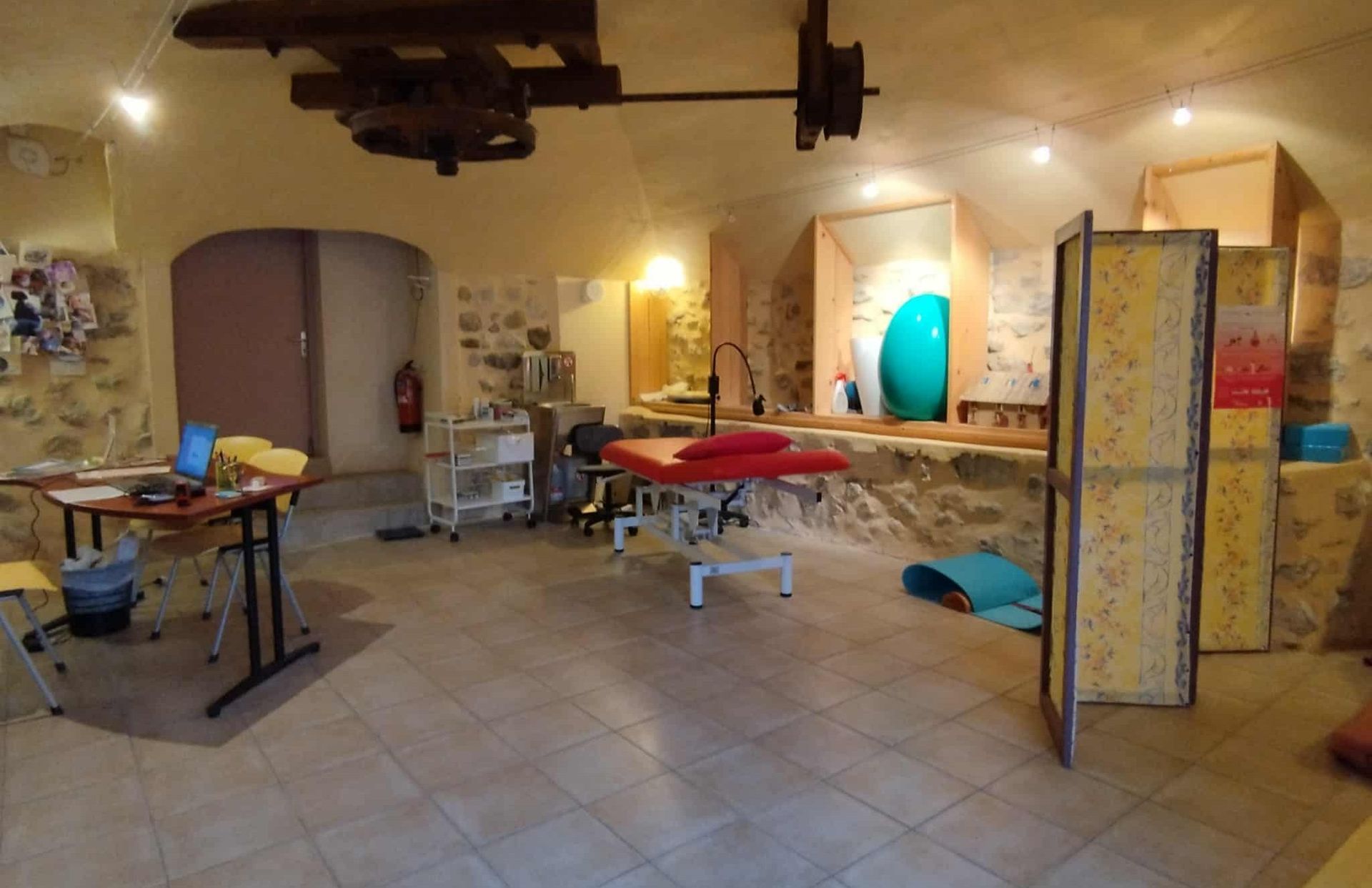 Intérieur d'une pièce avec des murs en pierre, une table de massage et diverses œuvres d'art.