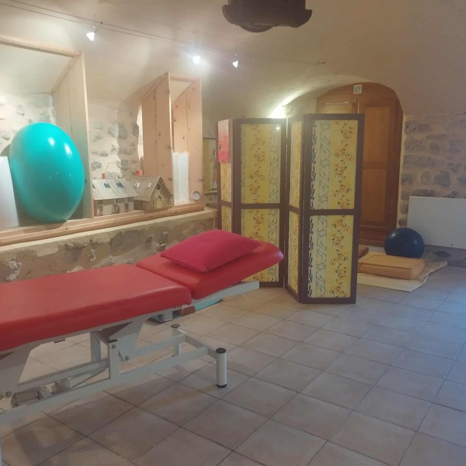 Intérieur de la salle de massage avec table rouge, ballon d'exercice bleu sarcelle et écran de confidentialité.