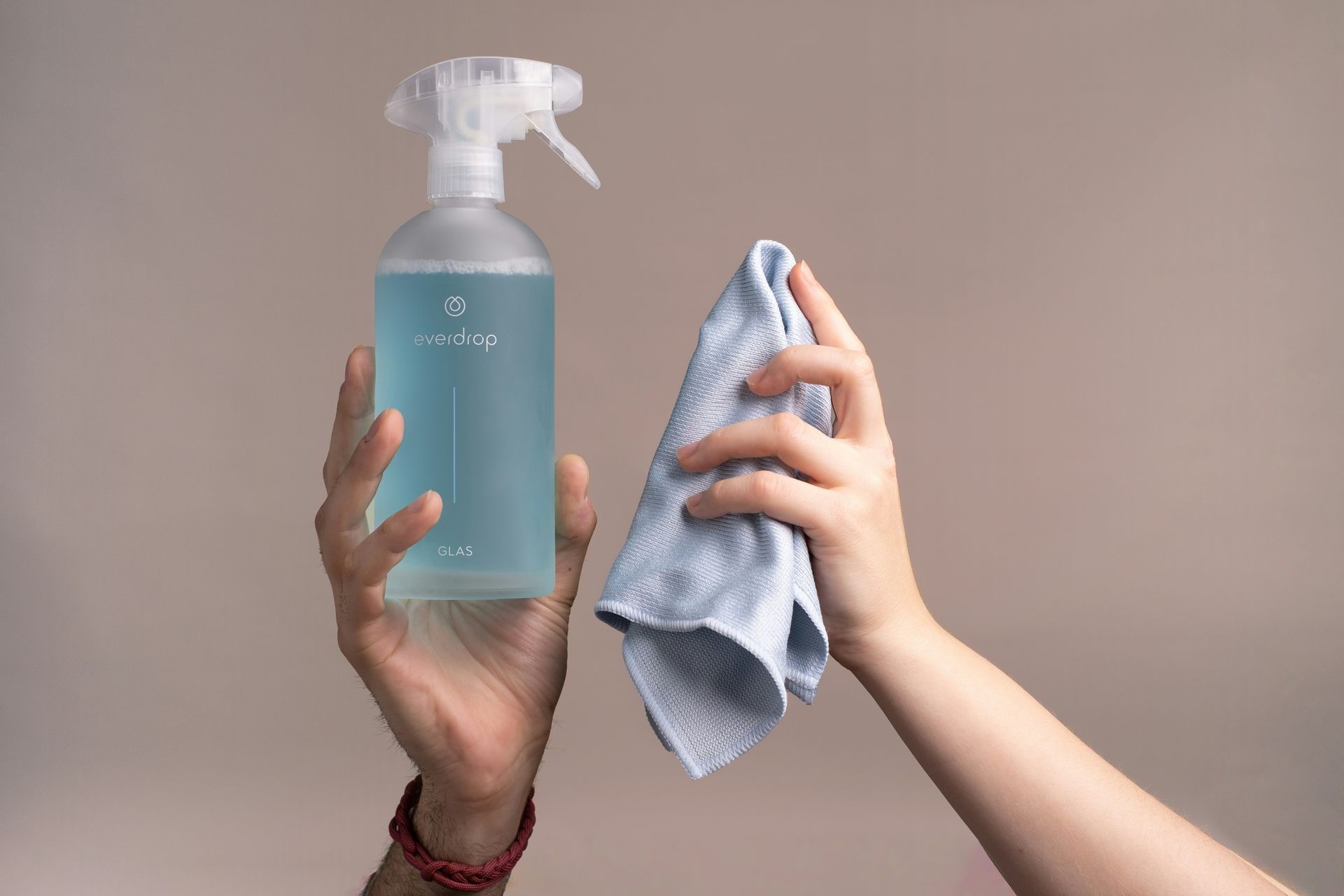 Des mains tenant un vaporisateur bleu et un chiffon de nettoyage gris sur un fond uni