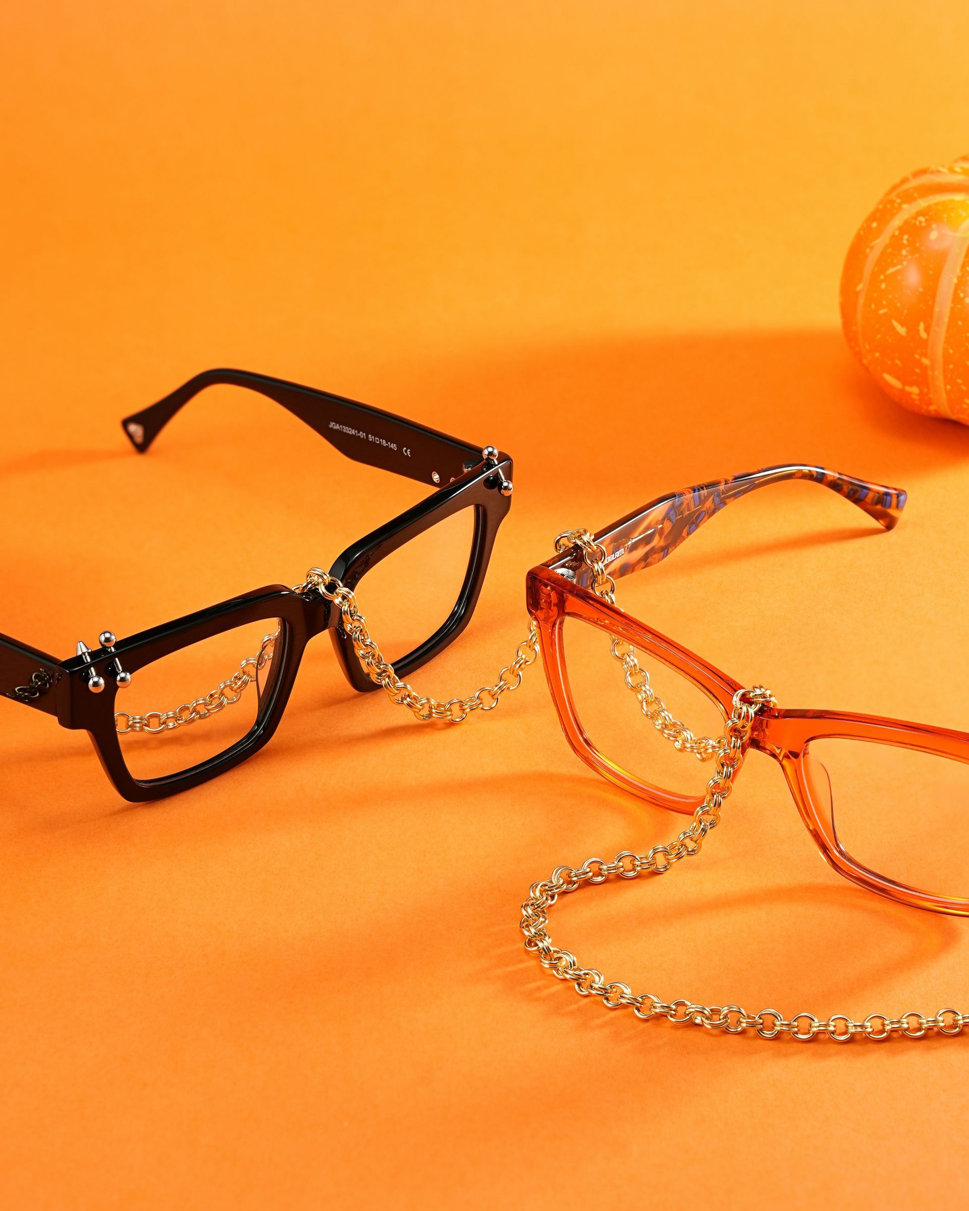Deux montures de lunettes, l’une noire et l’autre orange, sur un fond orange avec une petite citrouille