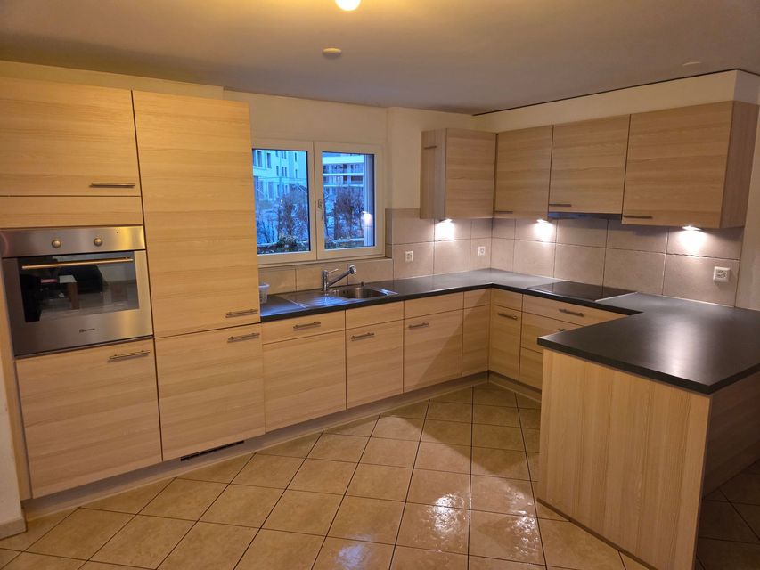 Cuisine beige clair avec placards en bois, plans de travail noirs et fenêtre au-dessus de l'évier.