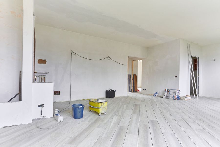 Pièce blanche vide en cours de rénovation, avec des seaux, des outils et une échelle au sol.