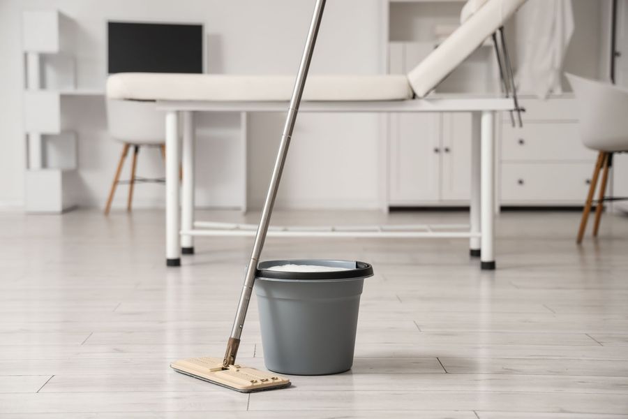 Balai et seau gris sur le sol blanc d'une cuisine dans une pièce lumineuse