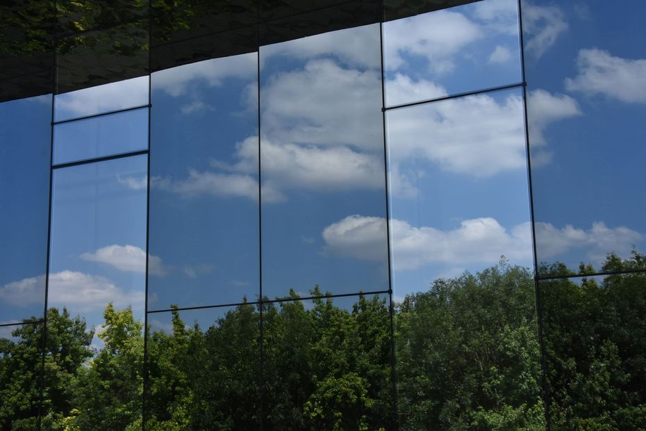 Bâtiment de verre reflétant le ciel bleu et les nuages ​​au-dessus des arbres verdoyants