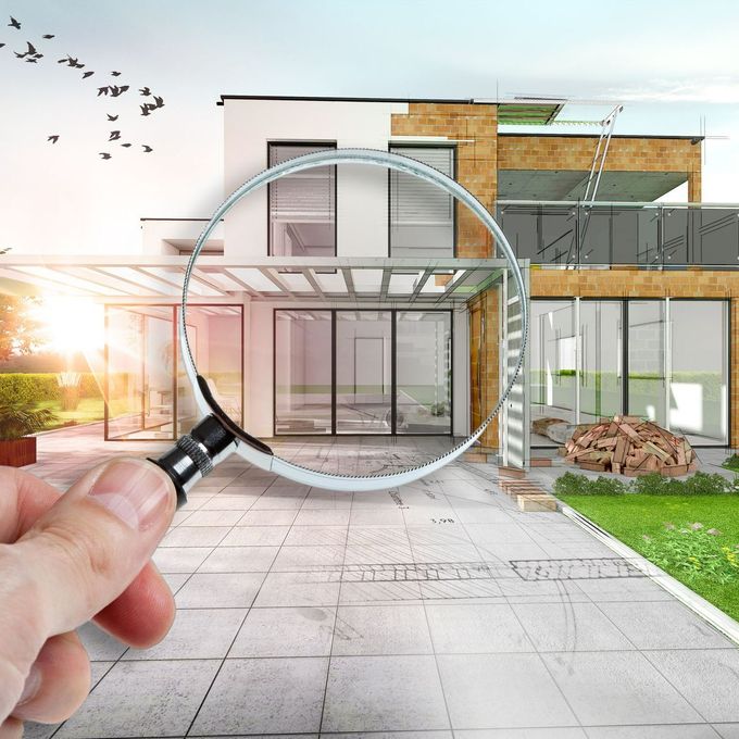 Une main tient une loupe sur un plan de maison.