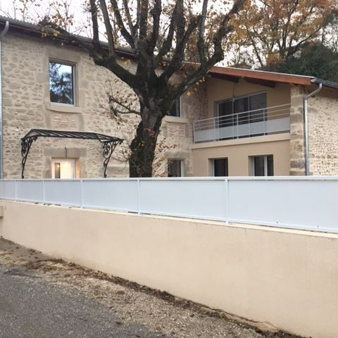 Maison en pierre derrière un muret avec une clôture.