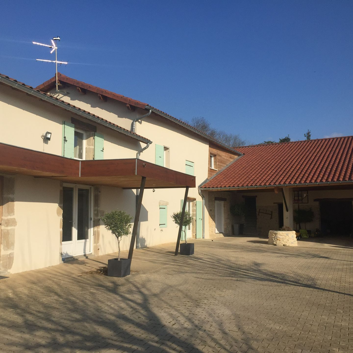 Maison rénovée avec des volets vert pastel et une cour.