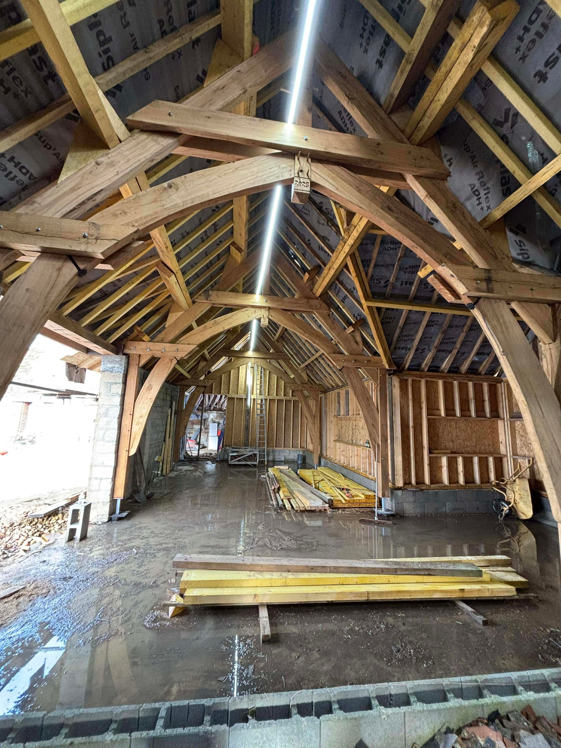 Intérieur d'une grange rustique avec poutres apparentes, murs en planches et matériaux de construction au sol.