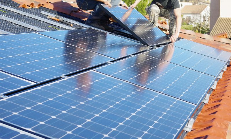 Des ouvriers installent des panneaux solaires sur un toit sous un soleil radieux.