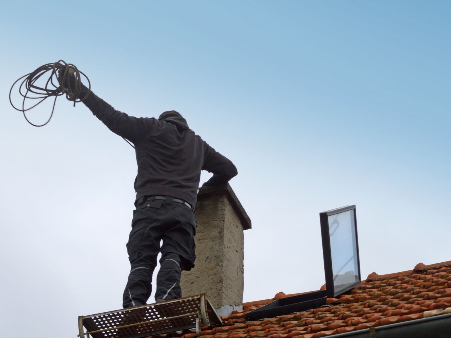 Ouvrier sur un toit, tenant un câble sur fond de ciel bleu clair