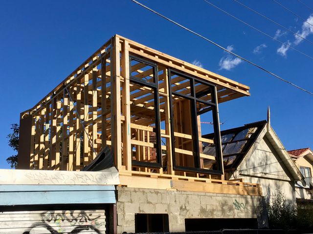 Maison partiellement construite avec une charpente en bois apparente sous un ciel bleu