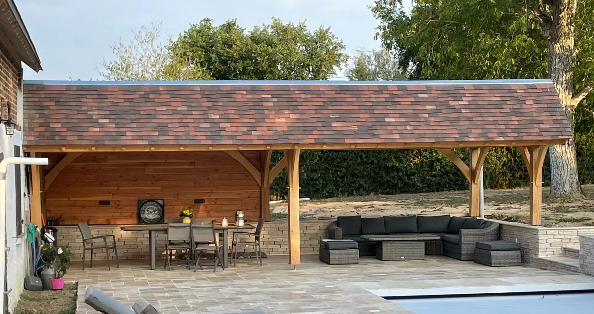 Terrasse couverte avec coin repas en bois et salon de jardin gris au bord de la piscine