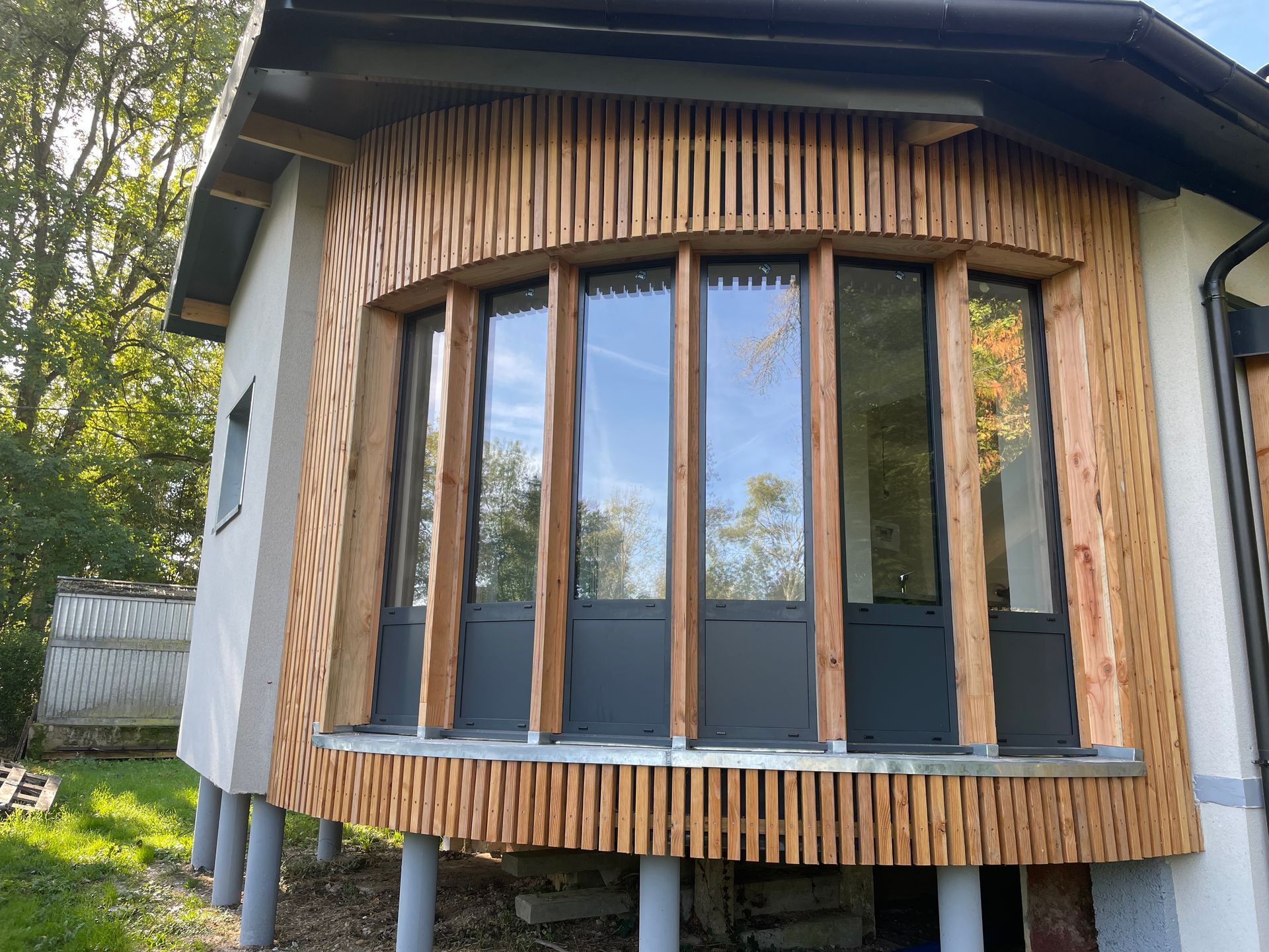 Baie vitrée cintrée avec garniture en lattes de bois sur l'extérieur d'une maison moderne