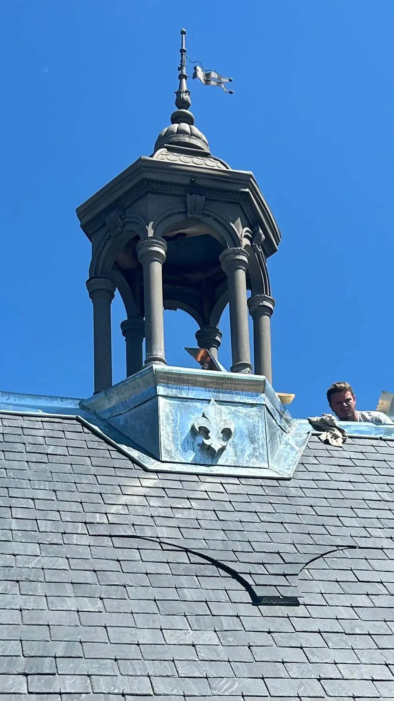 Toit en ardoise surmonté d'une petite coupole ornée, se détachant sur un ciel bleu limpide.