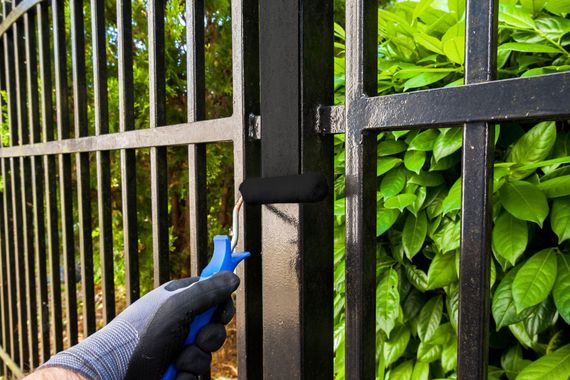 Une personne peint un portail en métal noir au rouleau à peinture.