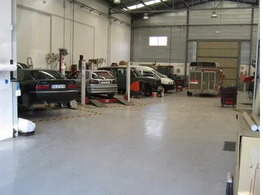 Automóviles en ascensores dentro de un luminoso taller de reparación de automóviles; interior gris y blanco.