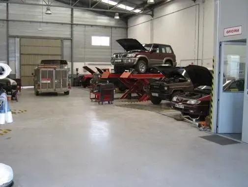 Interior de garaje con vehículos en elevadores, mecánico trabajando.