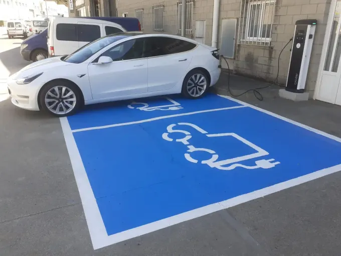 Un Tesla blanco cargándose en una estación de carga de vehículos eléctricos azul marcada.
