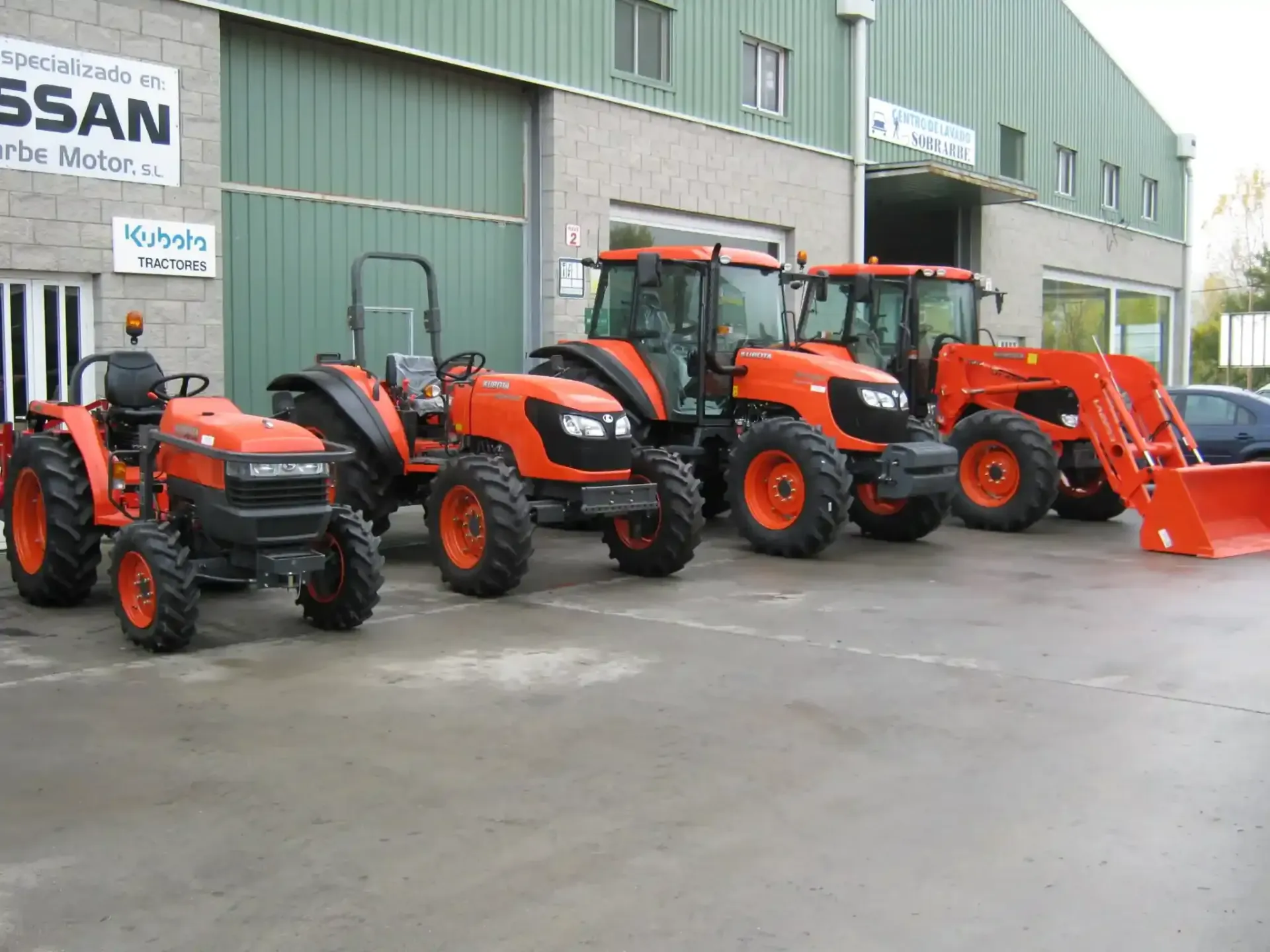 Tractores Kubota de color naranja alineados frente a un edificio con un cartel de Nissan.