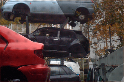 Coches apilados en un depósito de chatarra; coche rojo en primer plano, coches negros y plateados en el fondo.