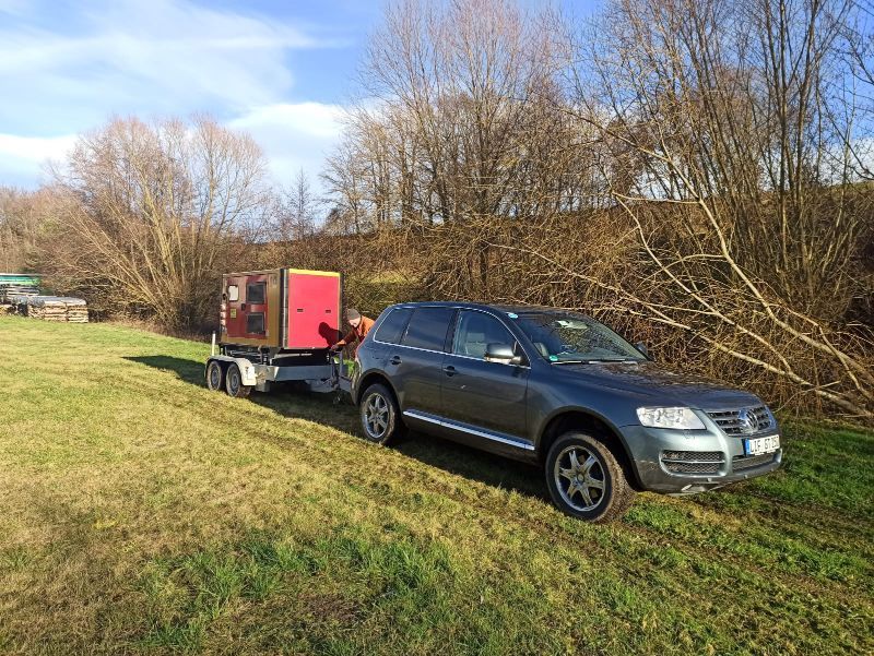 Auto mit Anhänger von Tribale Günter Mobiles Sägewerk auf einer Wiese
