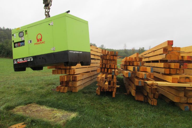 Kran hebt eine Maschine, im Hintergrund geschnittenes Holz von Tribale Günter Mobiles Sägewerk