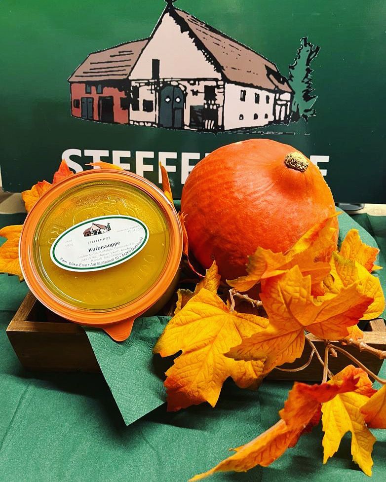 Ein Glas Suppe steht auf einem Tisch neben einem Kürbis und Blättern