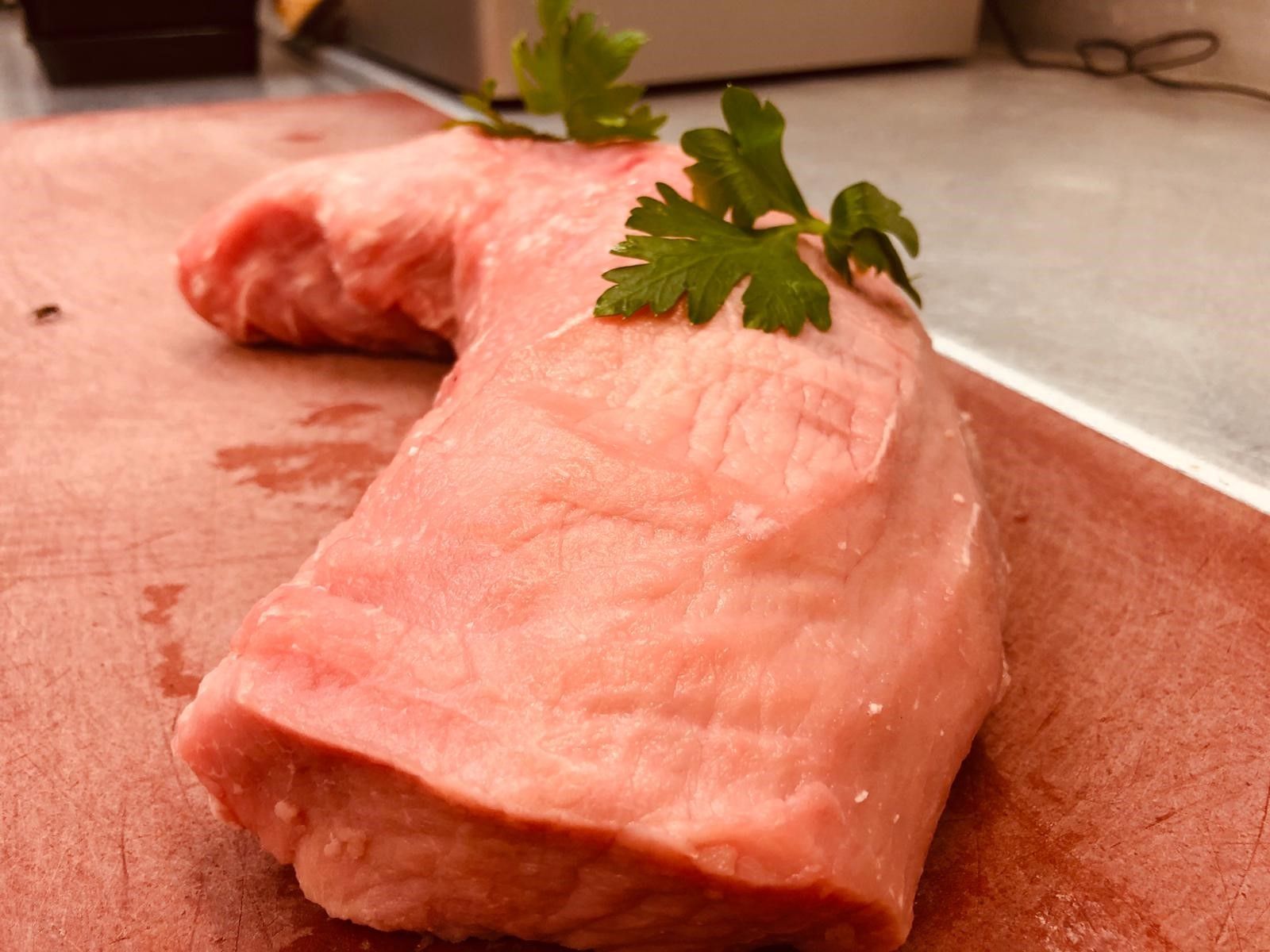 Ein Stück rohes Fleisch liegt auf einem roten Schneidebrett.