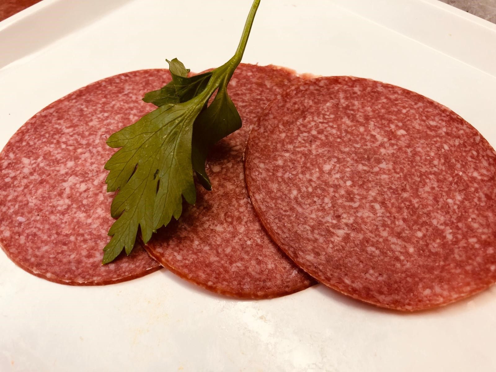 Drei Scheiben Salami Wurst auf einem weißen Teller mit Petersilie