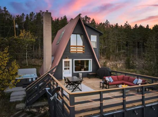 Patio with blue seating, fire pit, hot tub under a wooden pergola with corrugated roofing.