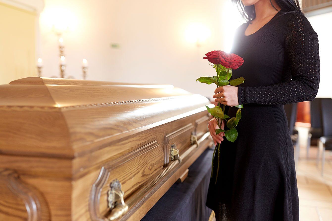Femme qui se recueille devant un cercueil avec une rose à la main