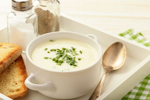 Eine Schüssel Suppe mit einem Löffel und Toast auf einem Tablett.