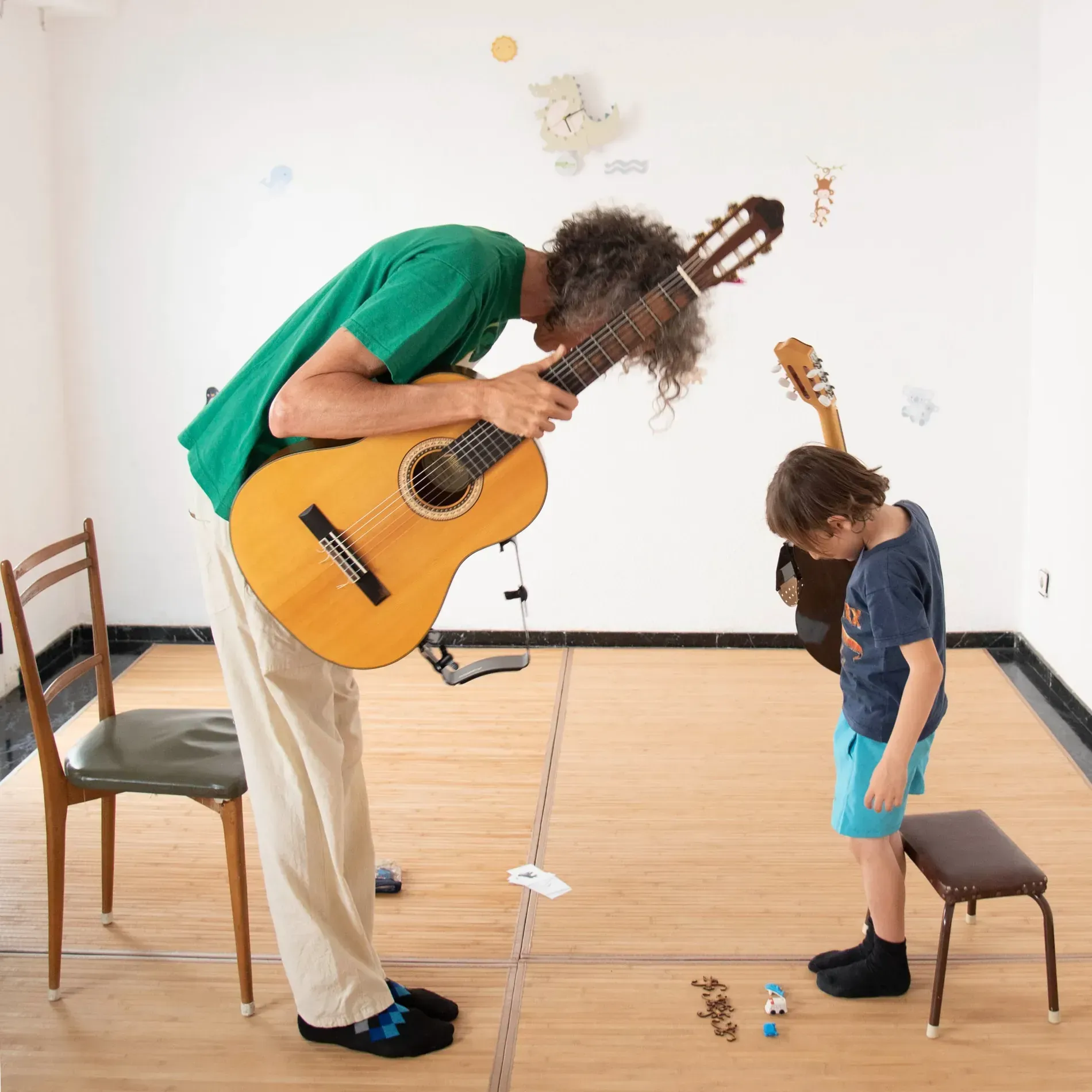 Un hombre con una camisa verde toca la guitarra para un niño pequeño.