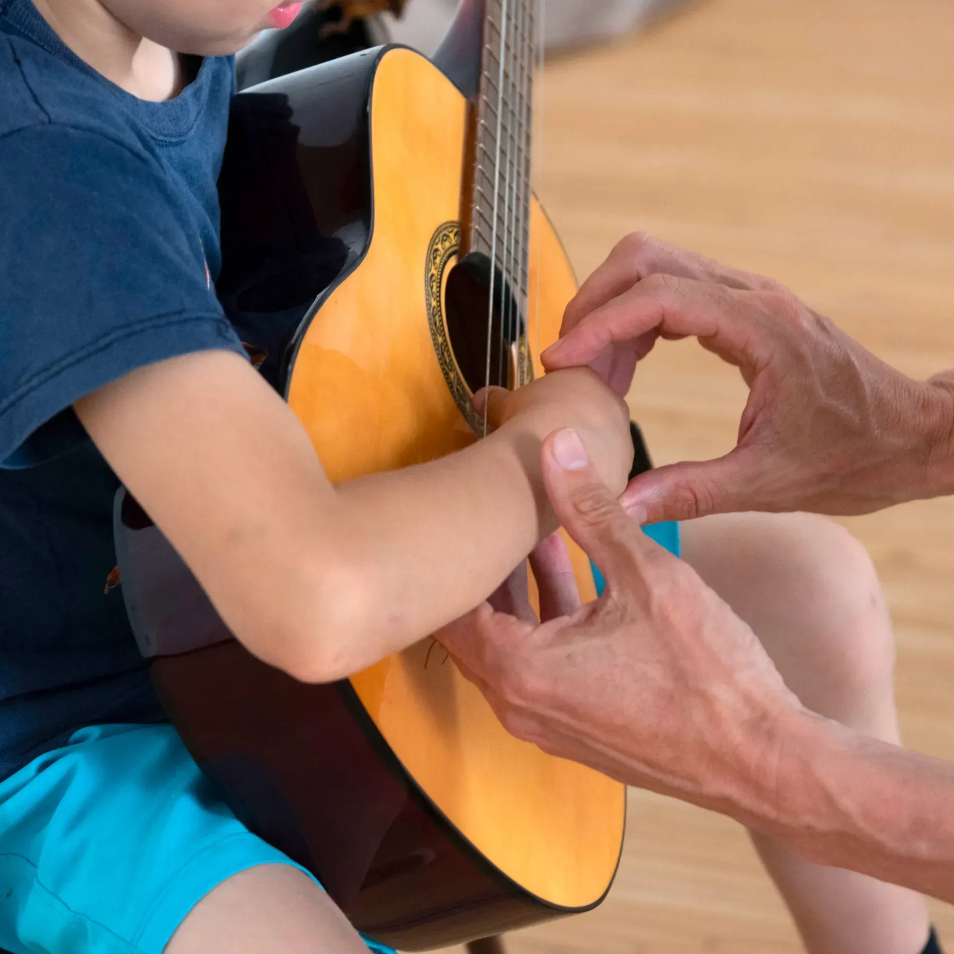 Una persona está ayudando a un niño pequeño a tocar una guitarra acústica.