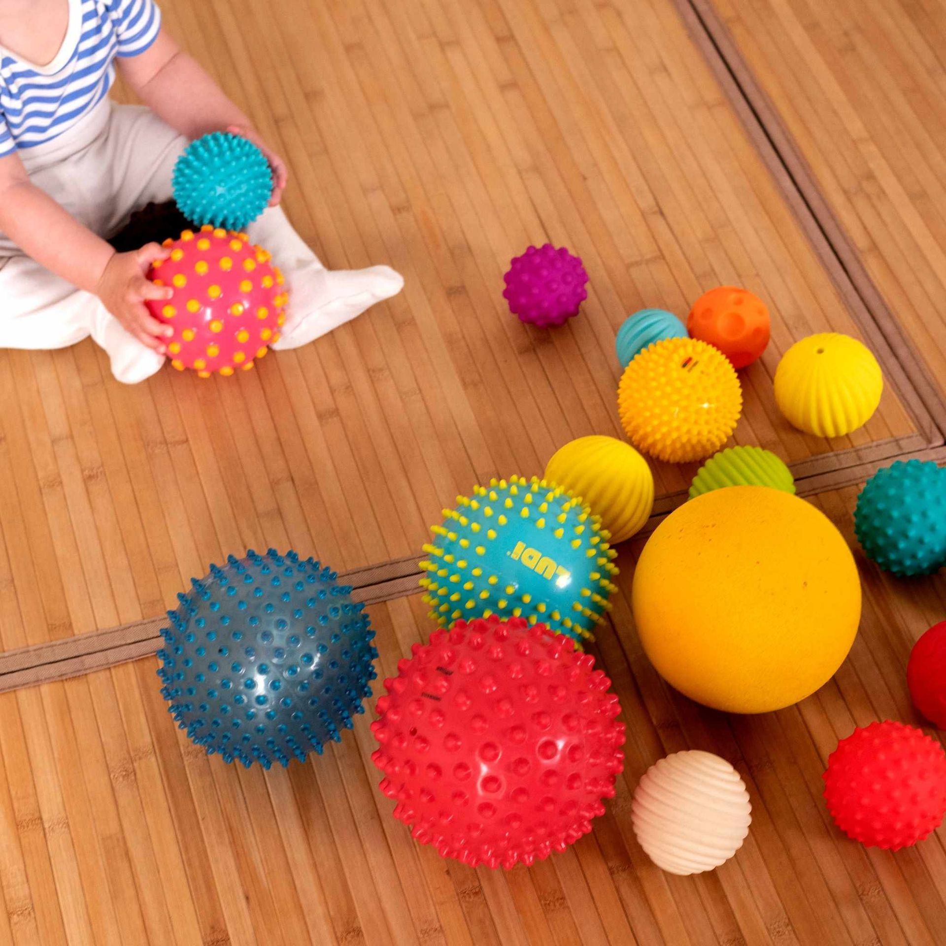 Un niño está sentado en el suelo jugando con pelotas, incluida una que dice saltar.