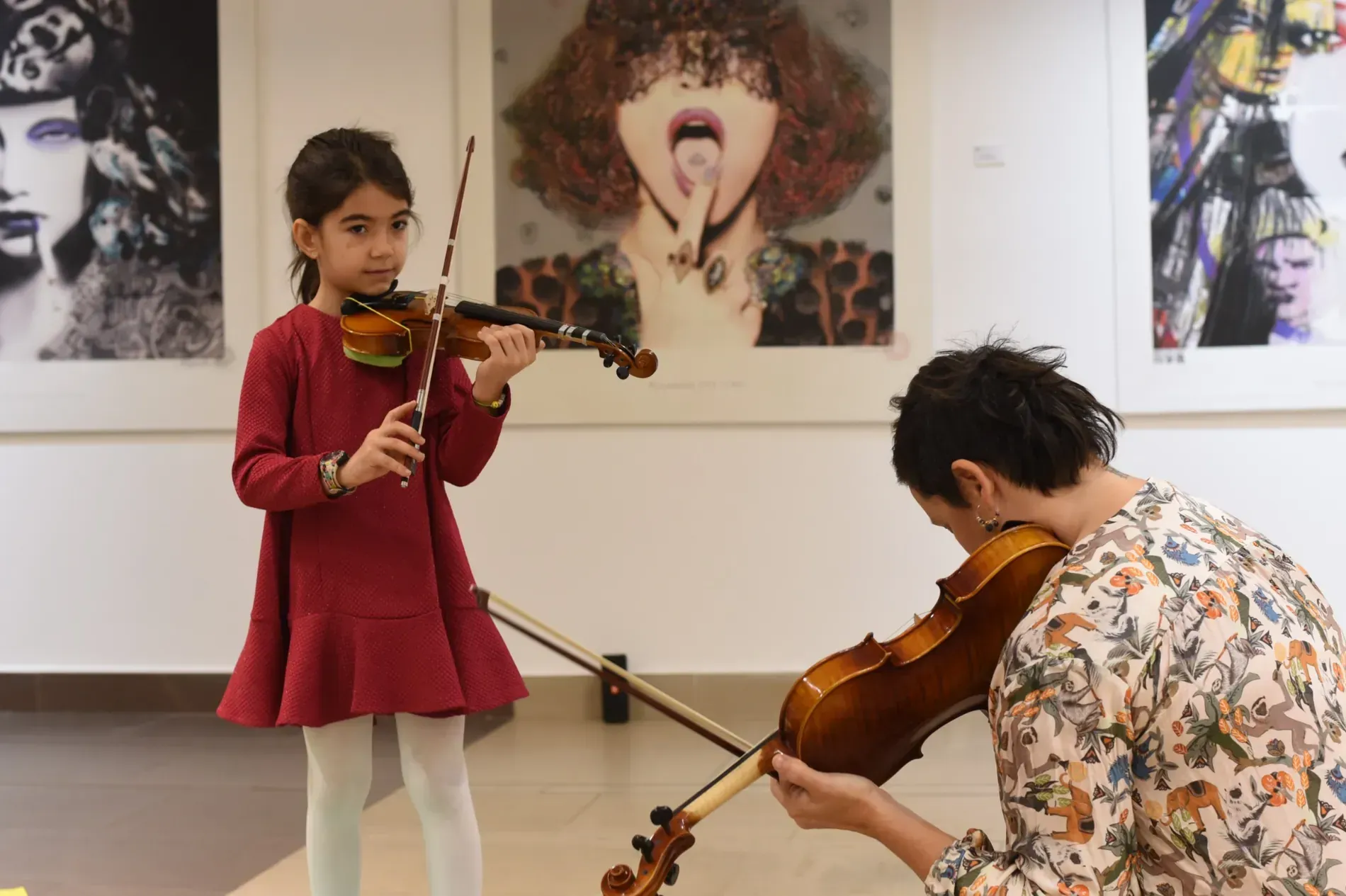Una niña está tocando un violín delante de un hombre que también toca un violín.